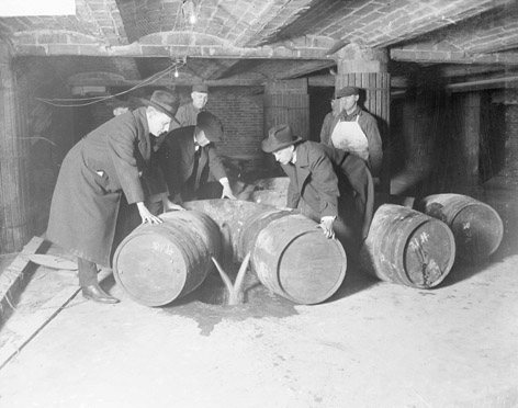 Männer gießen Alkohol aus Fässern in ein im Boden eingebautes Loch