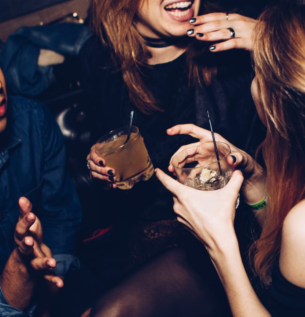 Zwei Frauen frühen Alters sind auf einer Feier und halten alkoholische Getränke in der Hand