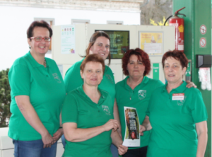 Fünf Frauen mittleren Alters in grüner Uniform an einer Tankstelle