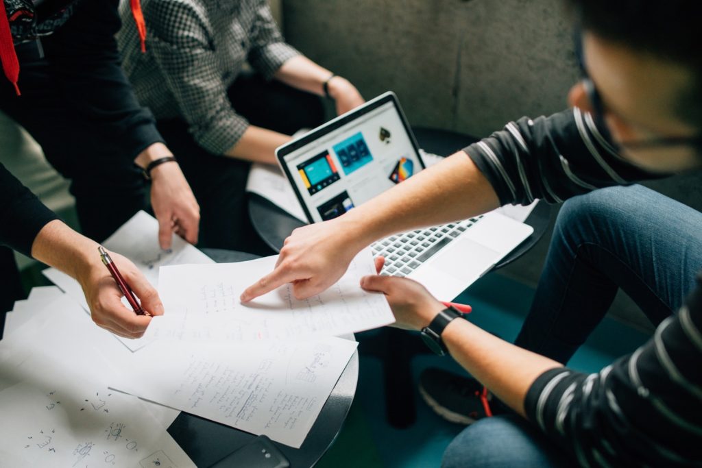 Eine gruppe von Personen arbeitet gemeinsam mit einem Laptop und Notizen auf Papier