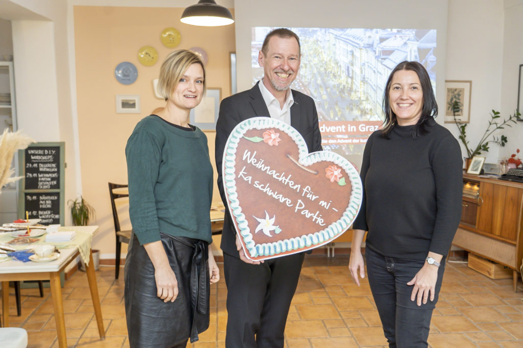 Drei Personen, die mittlere hält ein Lebkuchenherz mit der Aufschrift "Weihnachten für mi - ka schwere Partie