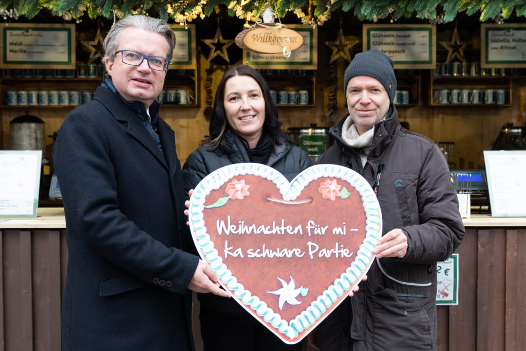 Drei Personen, die mittlere hält ein Lebkuchenherz mit der Aufschrift "Weihnachten für mi - ka schwere Partie