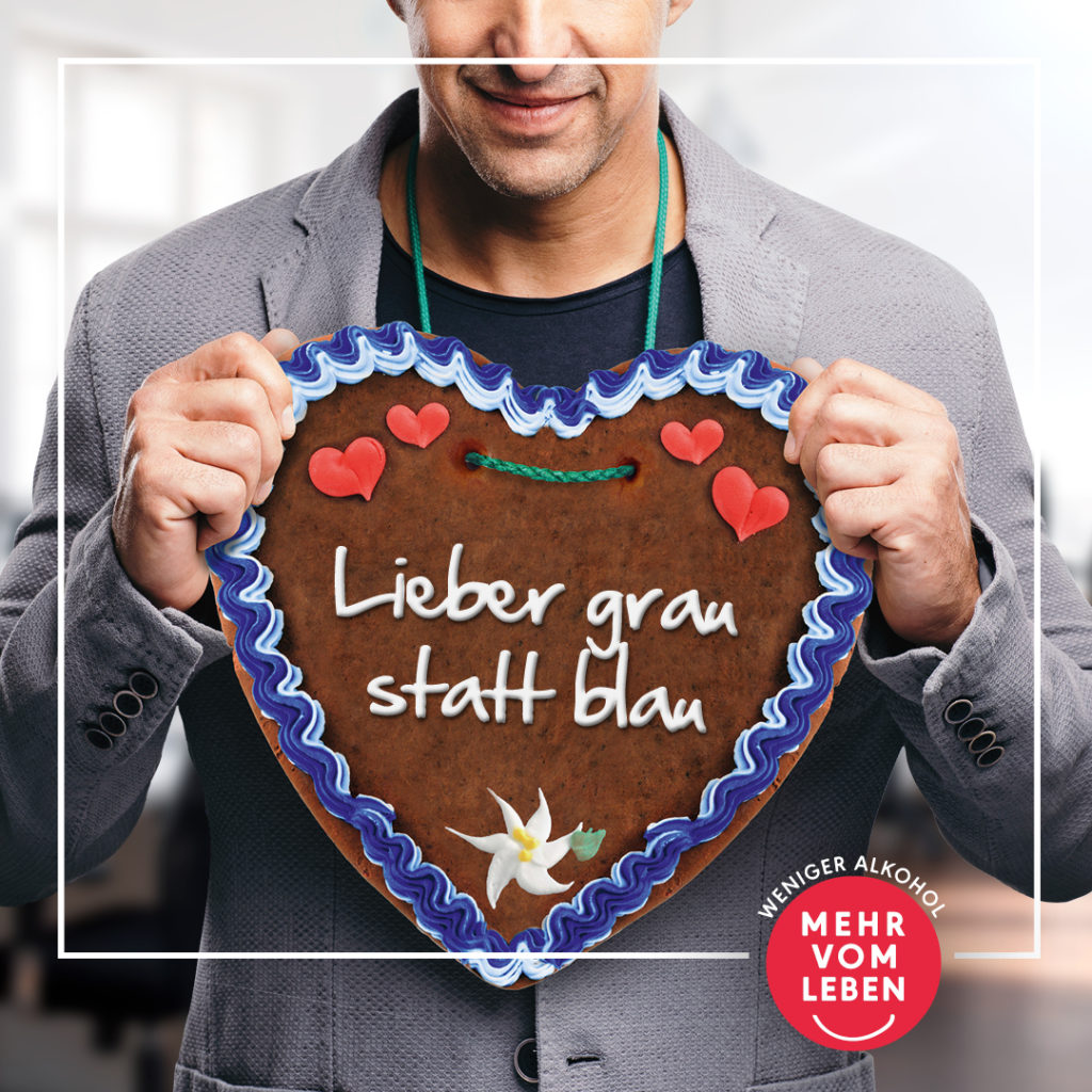 Ein Mann hält ein Lebkuchenherz mit der Aufschrift "Lieber grau statt blau" in der Hand