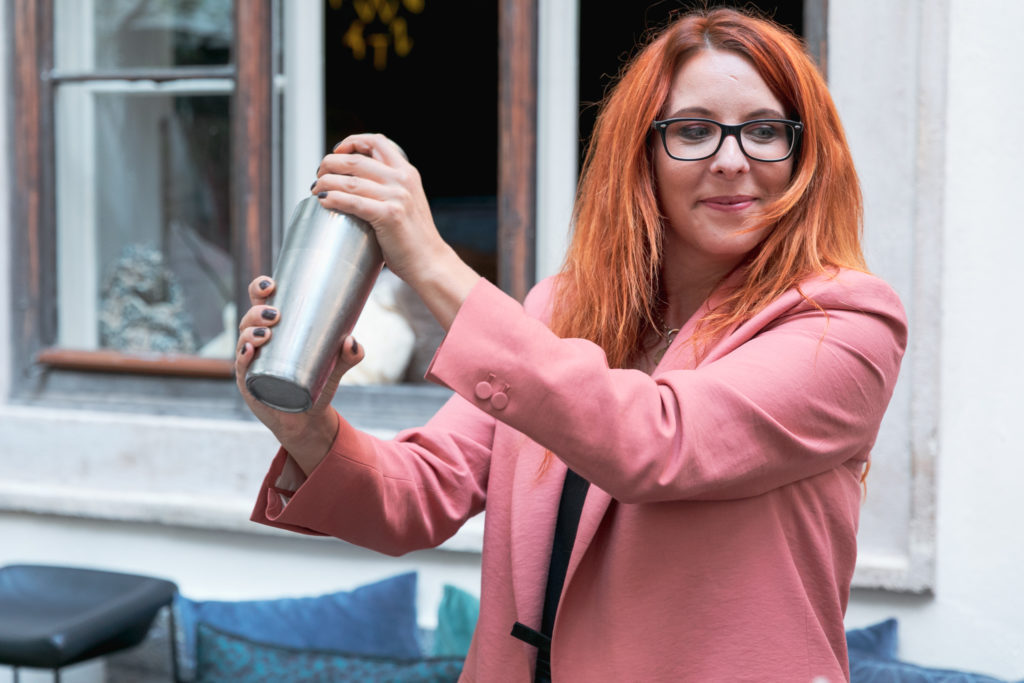 Frau mittleren Alters mit rosa Blazer shaket einen Mocktail.