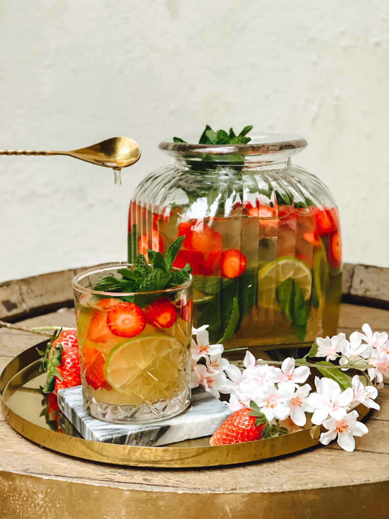 Erdbeerbowle in großem Glas, daneben abgefüllt in kleinem Glas gefüllt mit Erdbeeren, Minze und Limettenscheibe.