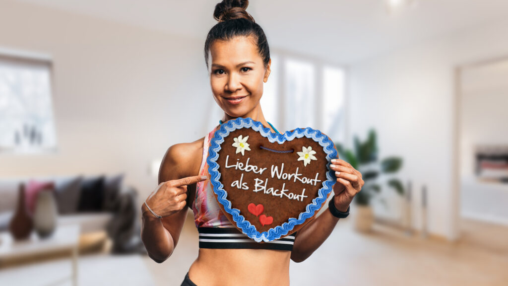 Frau mittleren Alters hält ein Lebkuchenherz mit der Aufschrift "Lieber Workout als Blackout"