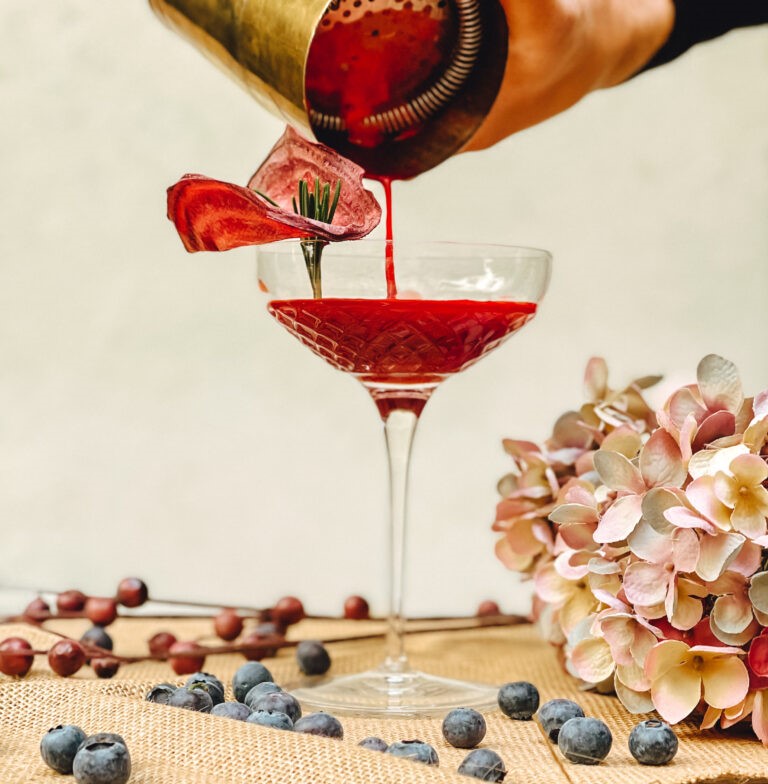 Heidelbeer-Rüben-Cocktail wird mit Shaker eingeschenkt.
