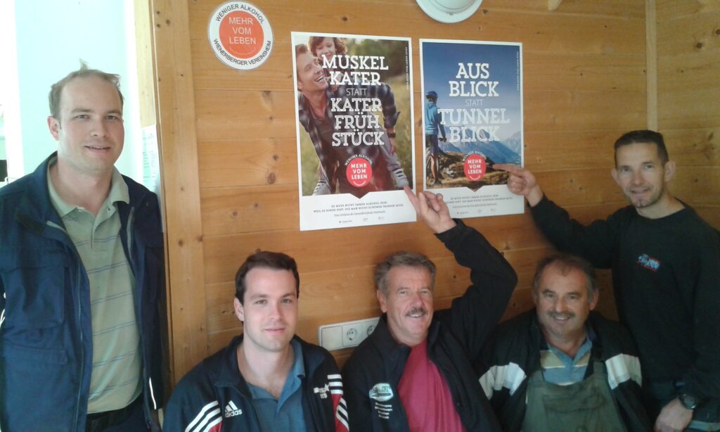 Fünf Männer vom Vereinshaus des USG Grambach zeigen auf Plakate der Initiative Weniger Alkohol - Mehr vom Leben"