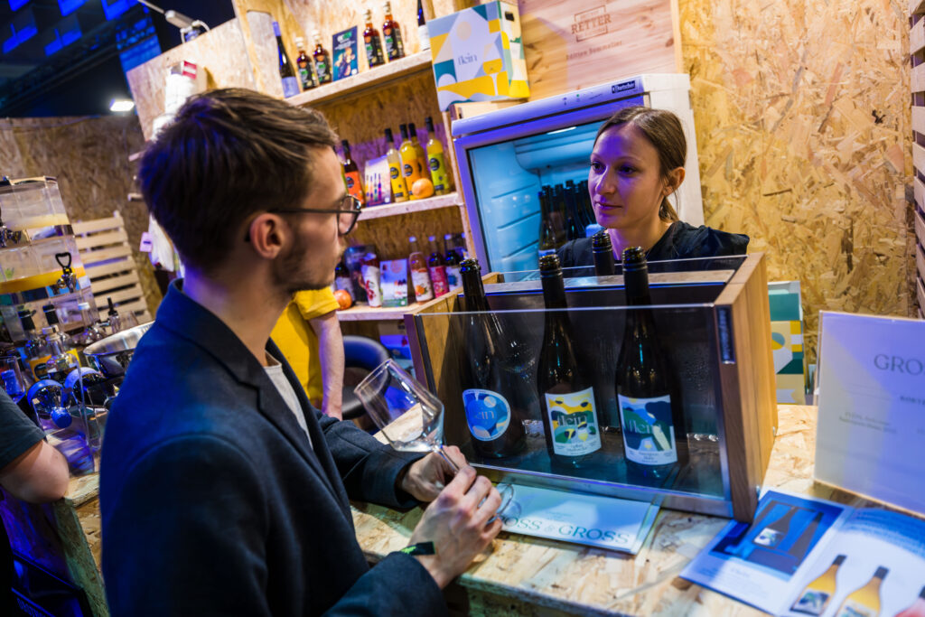 Bei einem Messestand lässt sich ein junger Herr von einer jungen Frau beraten. 